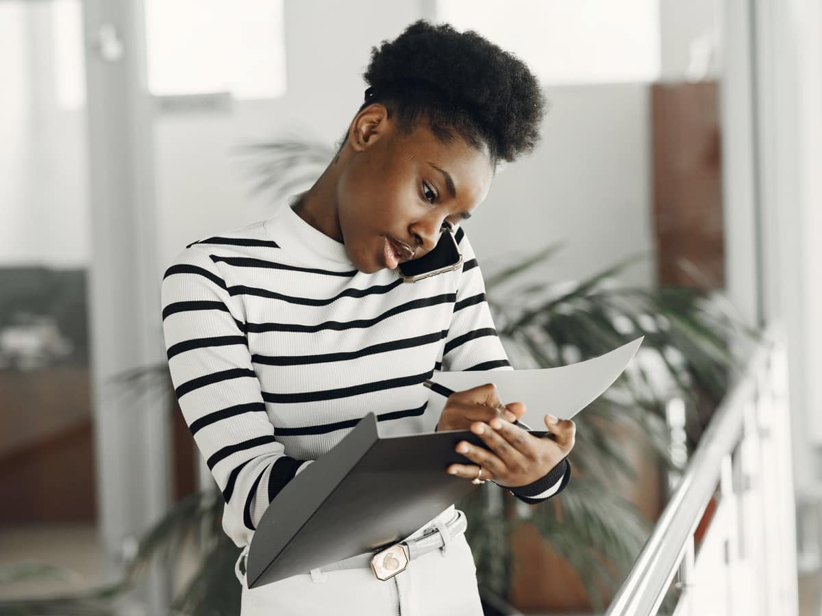 A woman on the phone, taking notes on a folder of documents